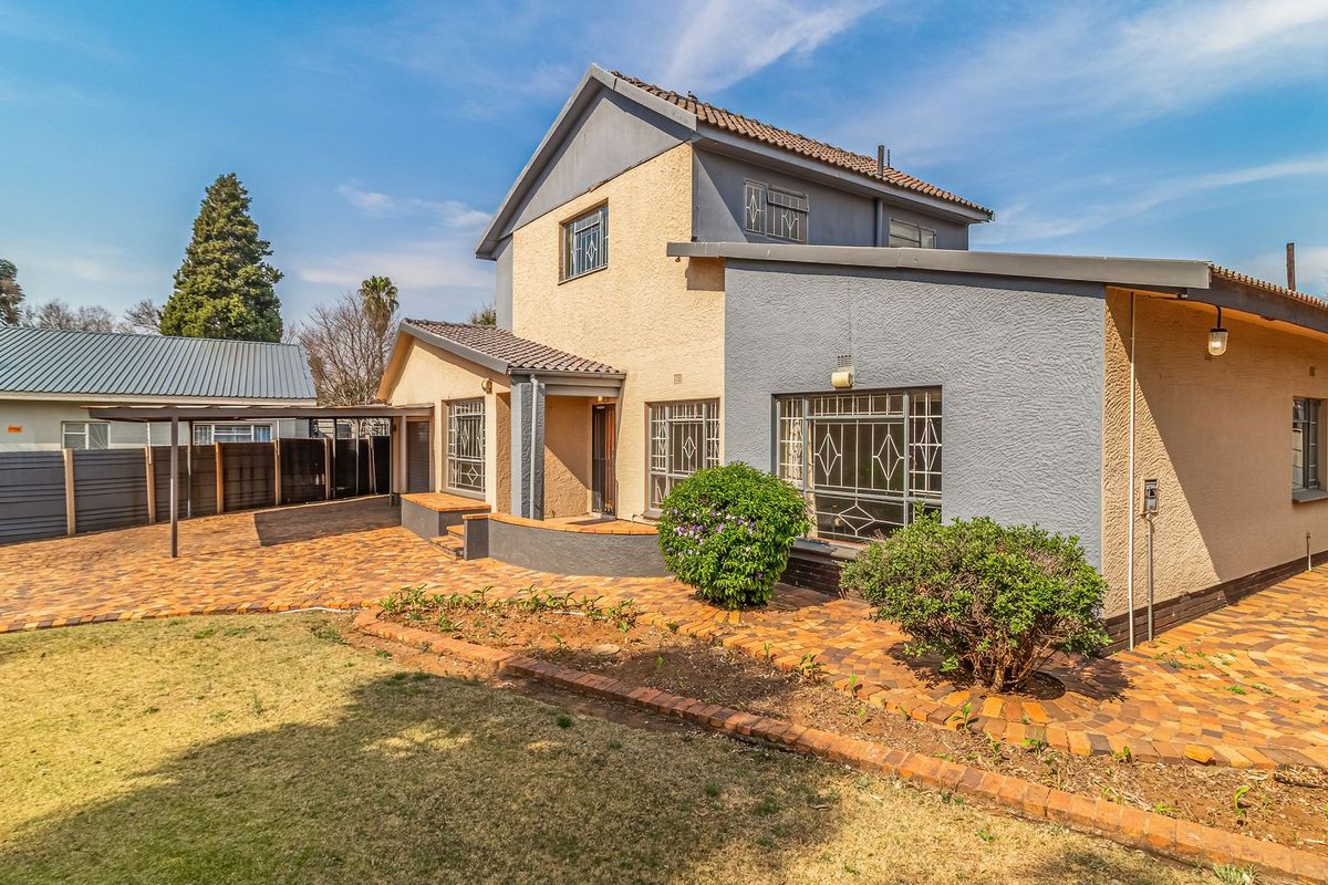 Rear view of the property featuring a paved courtyard, covered patio area, and established garden beds with security features on windows.