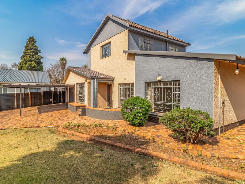 Rear view of the property featuring a paved courtyard, covered patio area, and established garden beds with security features on windows.