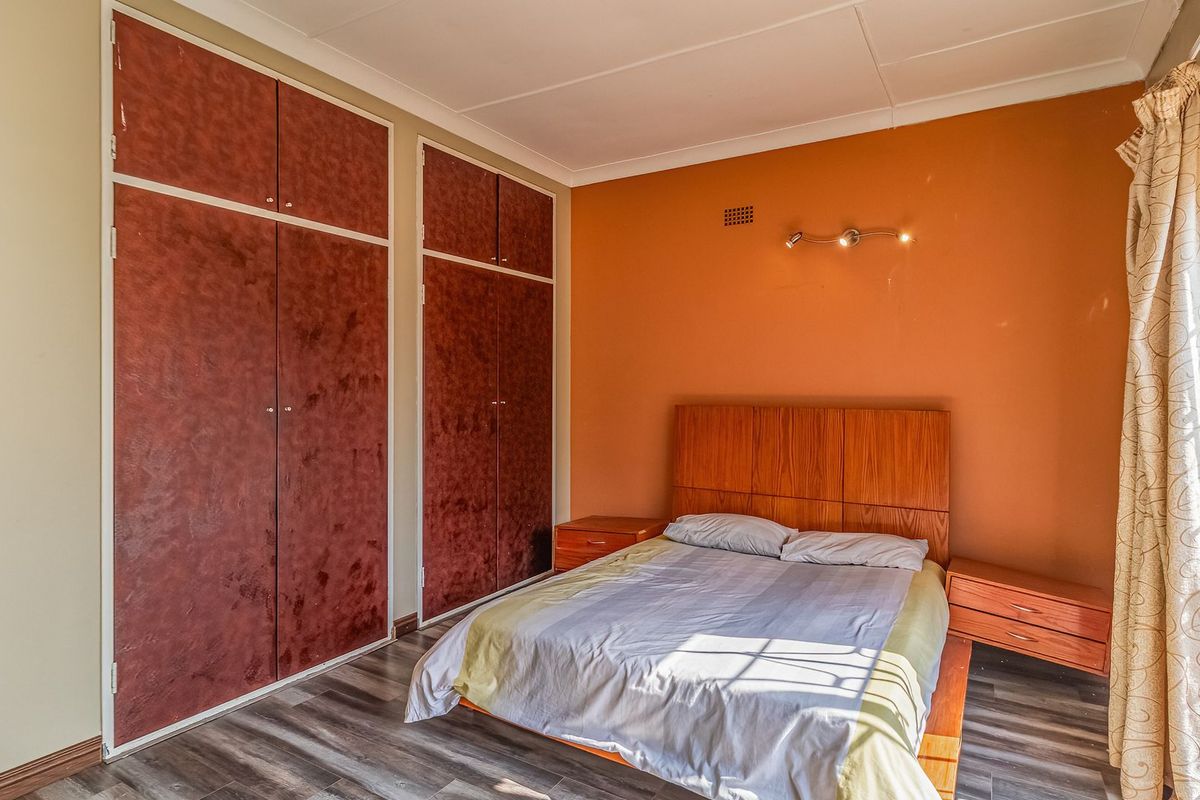 A bedroom featuring built-in cupboards, laminate flooring, and a wall-mounted light fixture, offering a functional space with potential for modern updates.