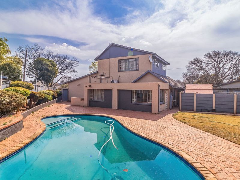 Rear exterior view of the house featuring a swimming pool, brick-paved patio area, and perimeter walling with electric fencing.