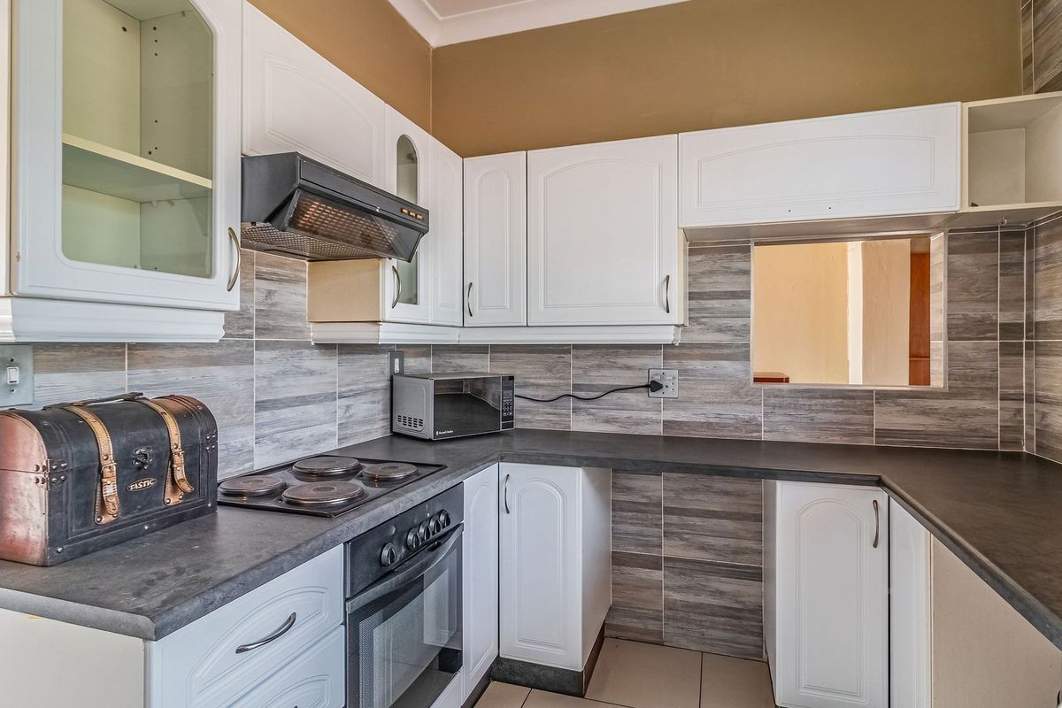 A functional kitchen featuring white cabinetry, dark laminate countertops, an electric hob, built-in oven, extractor fan, and modern wood-look tiled backsplash.