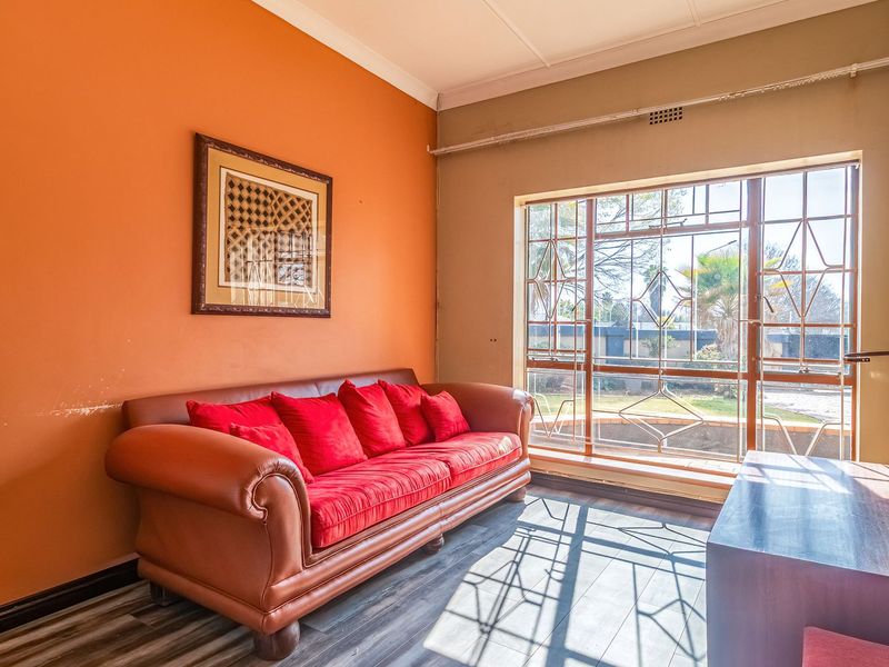 A living room featuring laminate flooring, a large window with security bars, and coving detail, offering natural light and potential for modern updates.