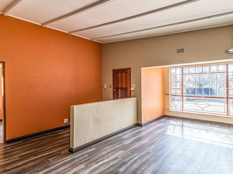 An empty living room featuring laminate flooring, exposed beam ceilings, and a built-in partition wall with access to an adjacent hallway.