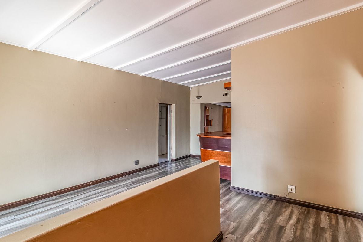 An empty living area featuring laminate flooring, exposed beam ceilings, and a built-in bar counter, offering a versatile space for renovation.