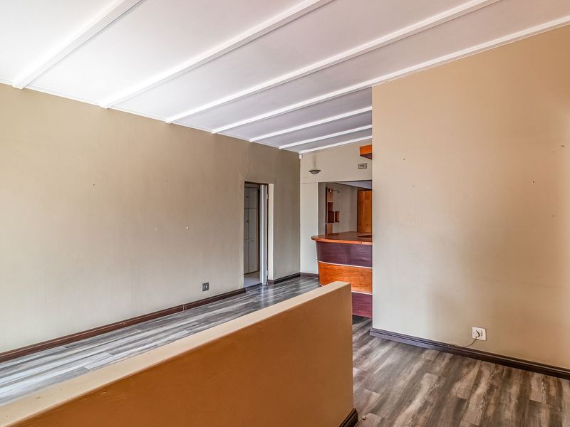 An empty living area featuring laminate flooring, exposed beam ceilings, and a built-in bar counter, offering a versatile space for renovation.