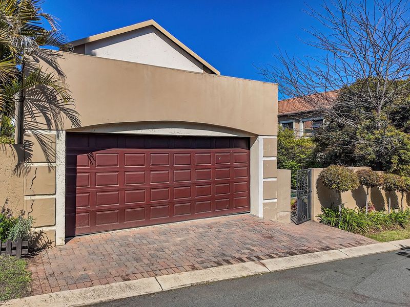 Front exterior view of the townhouse featuring a double garage, paved driveway, and secure pedestrian gate access.
