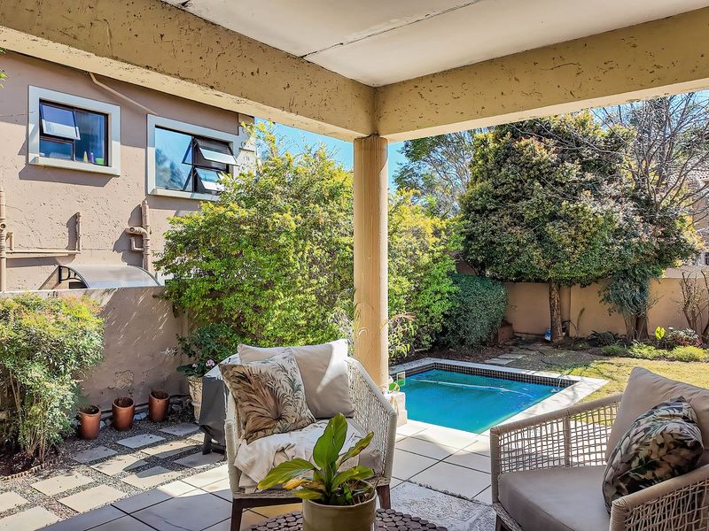 Covered patio area overlooking a private garden and swimming pool, featuring tiled flooring and structural concrete pillars.