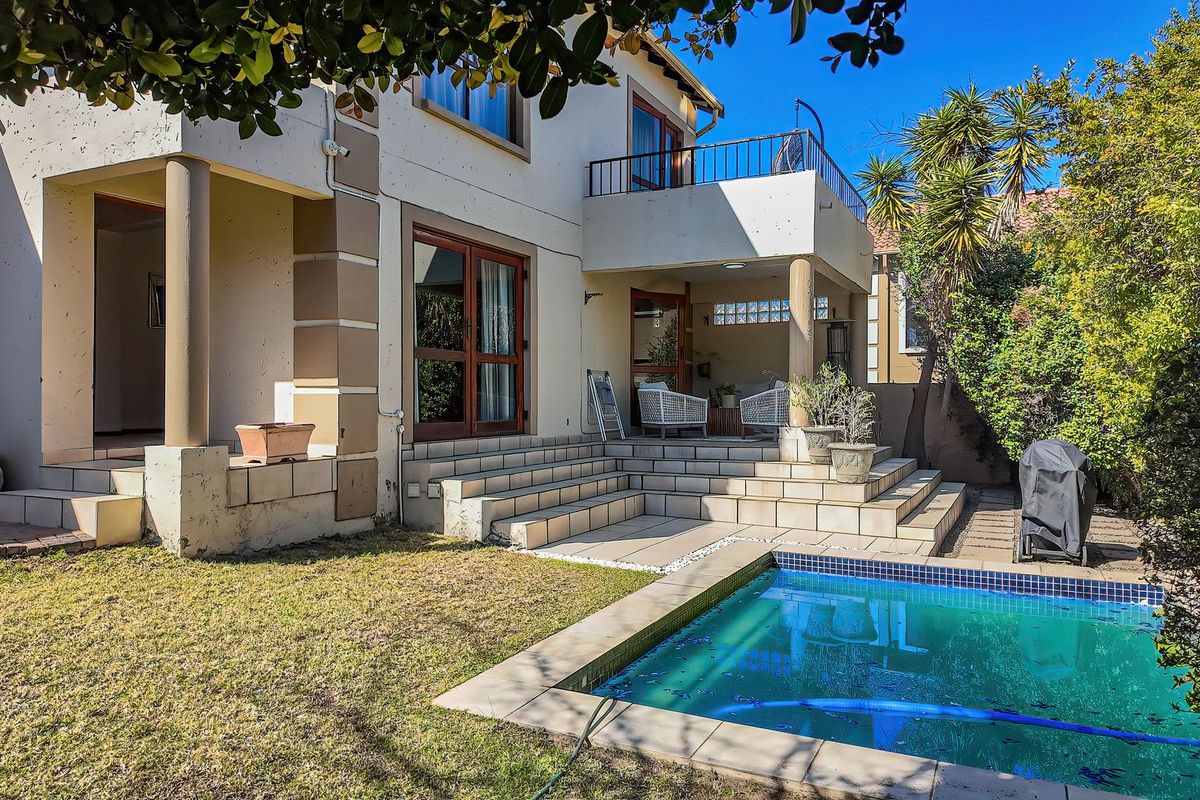 Rear exterior view of the townhouse featuring a tiled patio, swimming pool, and an upper-level balcony with metal railings.