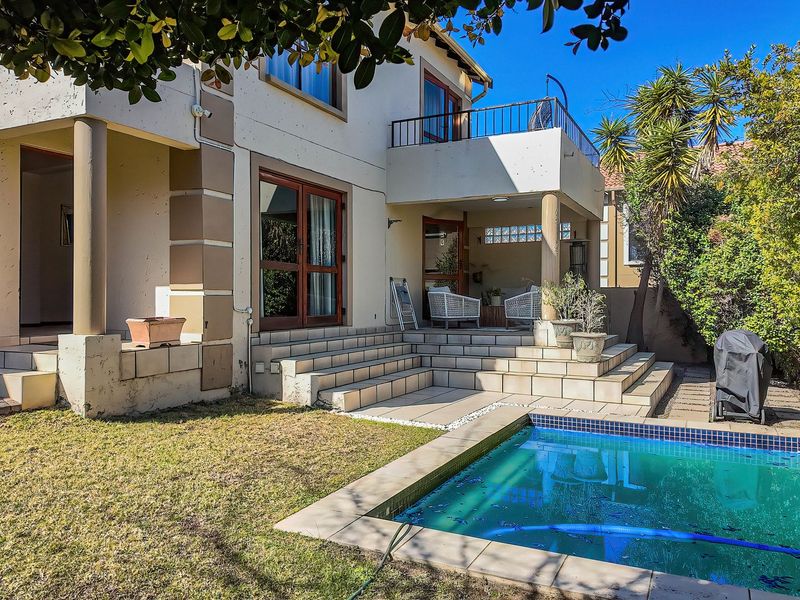 Rear exterior view of the townhouse featuring a tiled patio, swimming pool, and an upper-level balcony with metal railings.