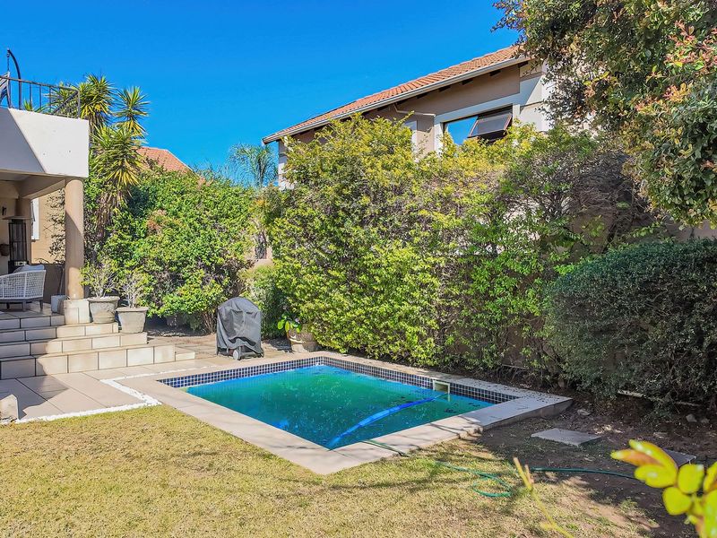 A private backyard featuring a swimming pool, a tiled patio area with stairs, and an elevated balcony overlooking the garden.