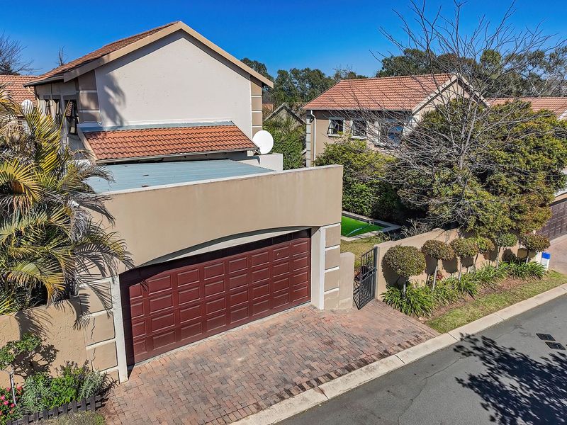 Elevated view of a townhouse exterior featuring a paved driveway, secure garage, and tiled roof structure within a residential complex.