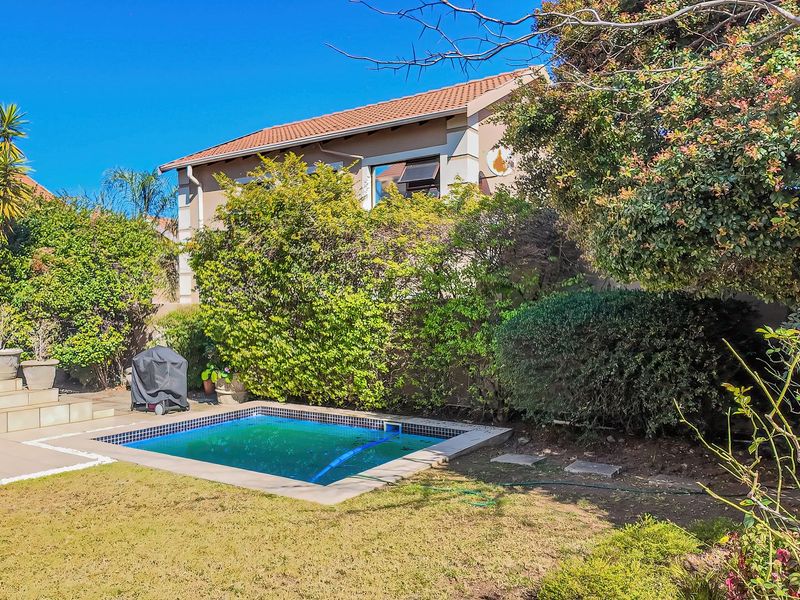 A private backyard featuring a small swimming pool, a paved patio area, and established garden landscaping adjacent to the townhouse structure.