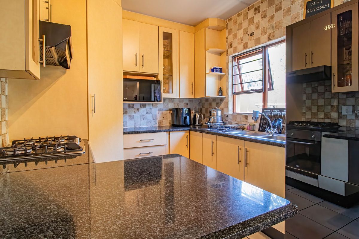 Functional kitchen featuring granite countertops, built-in cabinetry, gas hob, extractor fan, and a double sink with tiled backsplash.