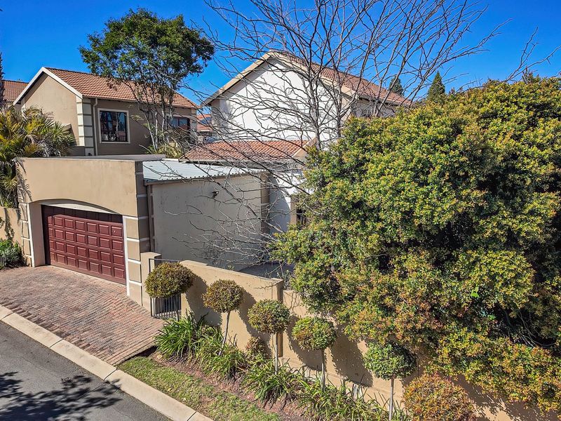 An elevated view of the townhouse exterior, featuring a brick driveway, a secure garage door, and established boundary wall landscaping.