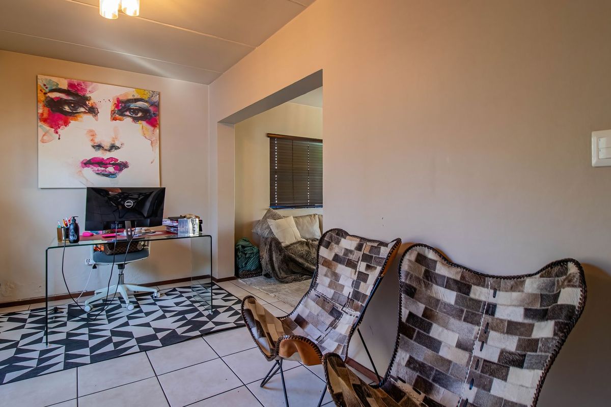 A living area featuring tiled flooring and a neutral wall finish, with an adjacent alcove space suitable for a home office or study nook.