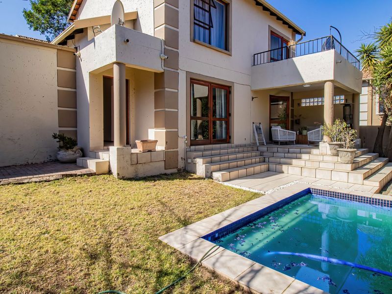 Rear view of the townhouse featuring a swimming pool, tiled patio area, and an upper-level balcony with access through sliding doors.