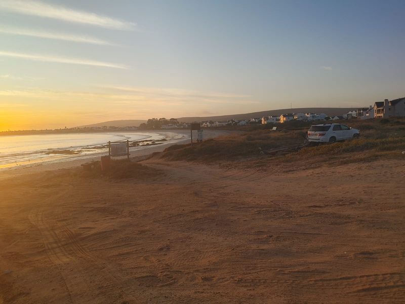 A scenic view of the coastline and beach area at sunset, showcasing the natural landscape and surrounding residential neighborhood.