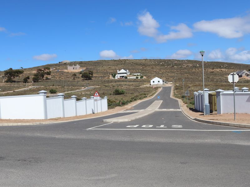A view of the paved street and surrounding residential development area, featuring established boundary walls and infrastructure.