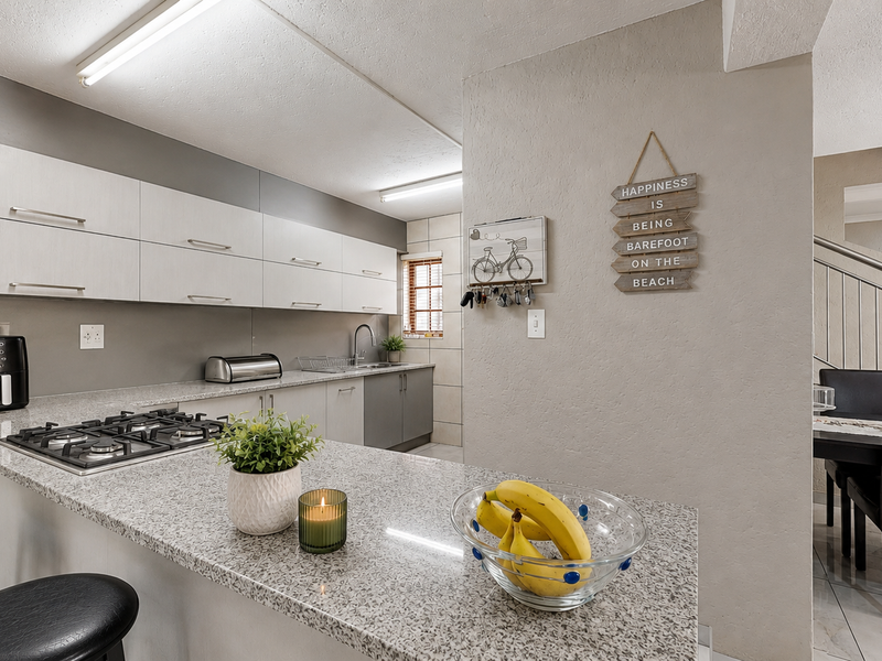 Modern open-plan kitchen featuring granite countertops, gas hob, and ample cabinetry, seamlessly flowing into the adjacent dining area with staircase access.