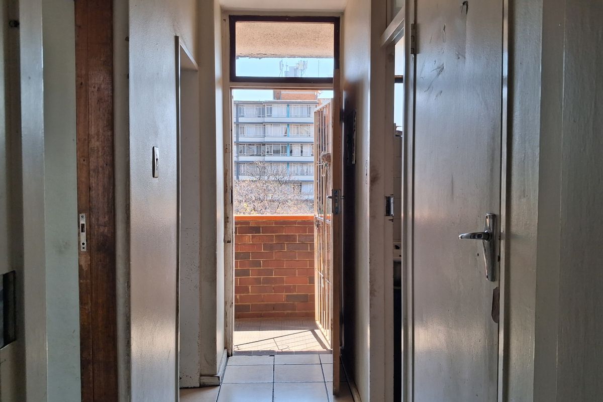A narrow interior hallway with tiled flooring, leading directly to an external balcony through a security gate.