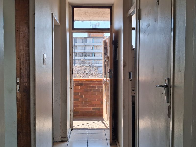 A narrow interior hallway with tiled flooring, leading directly to an external balcony through a security gate.