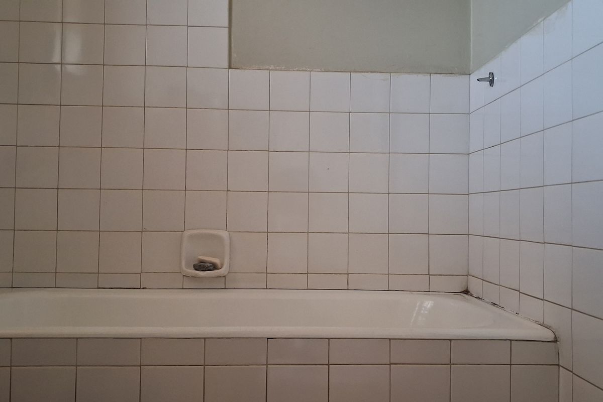 A dated bathroom featuring a built-in bathtub with white ceramic wall tiles and a recessed soap dish.