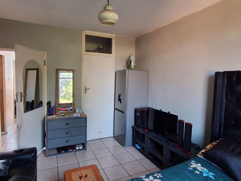 A bedroom featuring tiled flooring and a transom window above the door, showing signs of wear and requiring cosmetic updates.