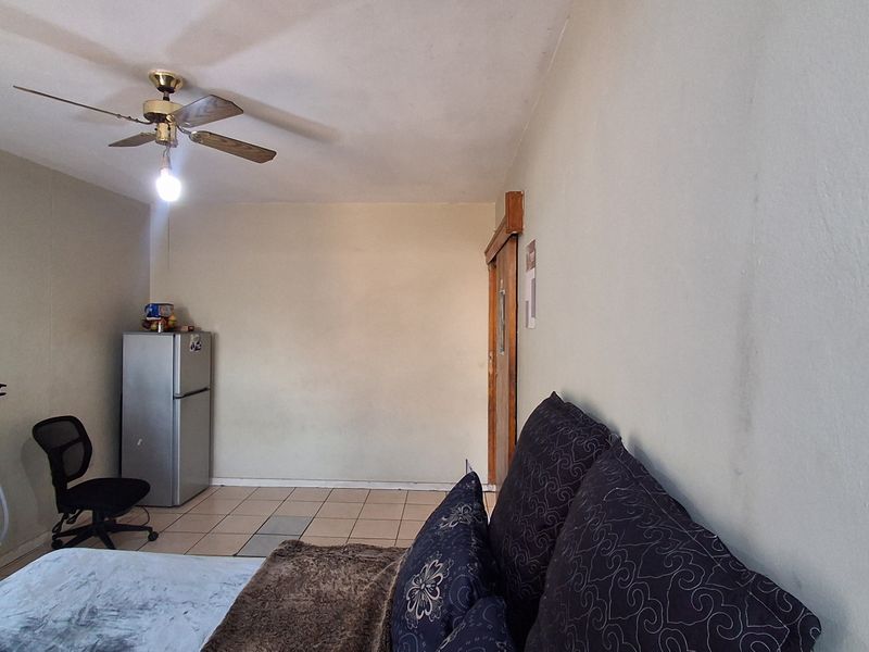 A bedroom featuring tiled flooring, a ceiling fan, and a sliding door, requiring cosmetic updates to the wall finishes.