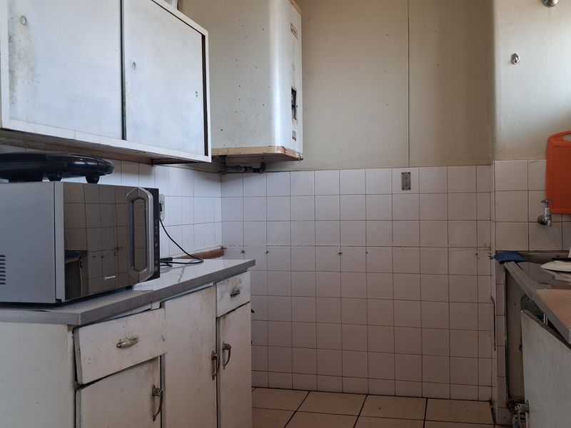 A dated kitchen area featuring original built-in cabinetry, a stainless steel sink, and wall-mounted geyser, requiring modernization and cosmetic updates.