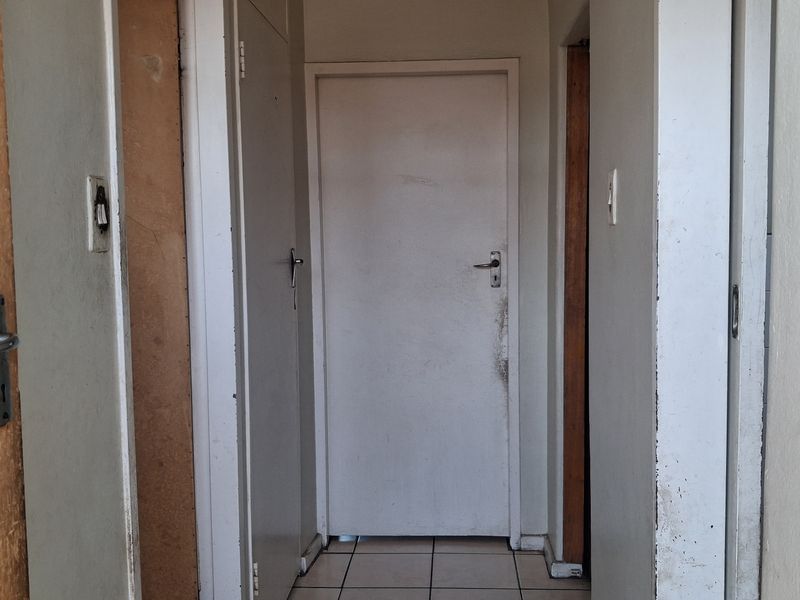 A narrow interior hallway featuring tiled flooring and multiple internal doors, showing signs of wear and requiring cosmetic updates to the paint and finishes.