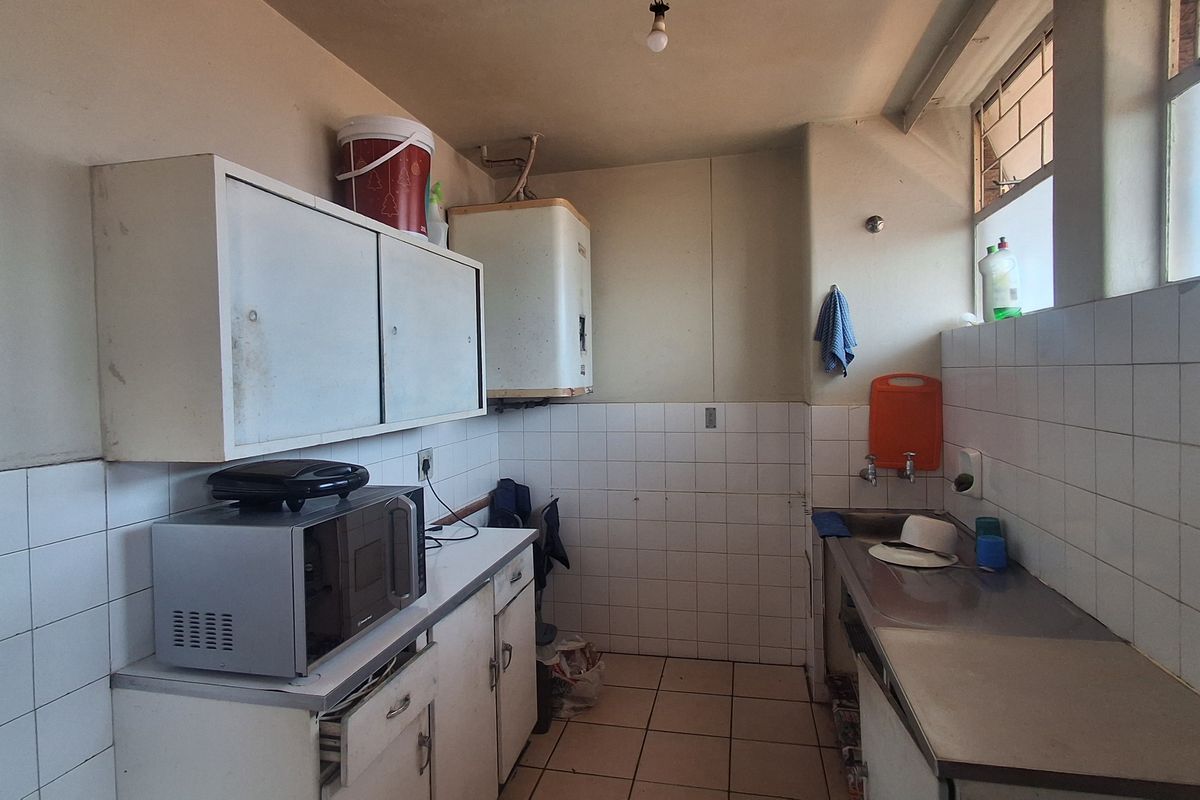 A functional kitchen area featuring tiled splashbacks, stainless steel sink, built-in cabinetry, and an electric geyser, requiring cosmetic updates to modernize the space.