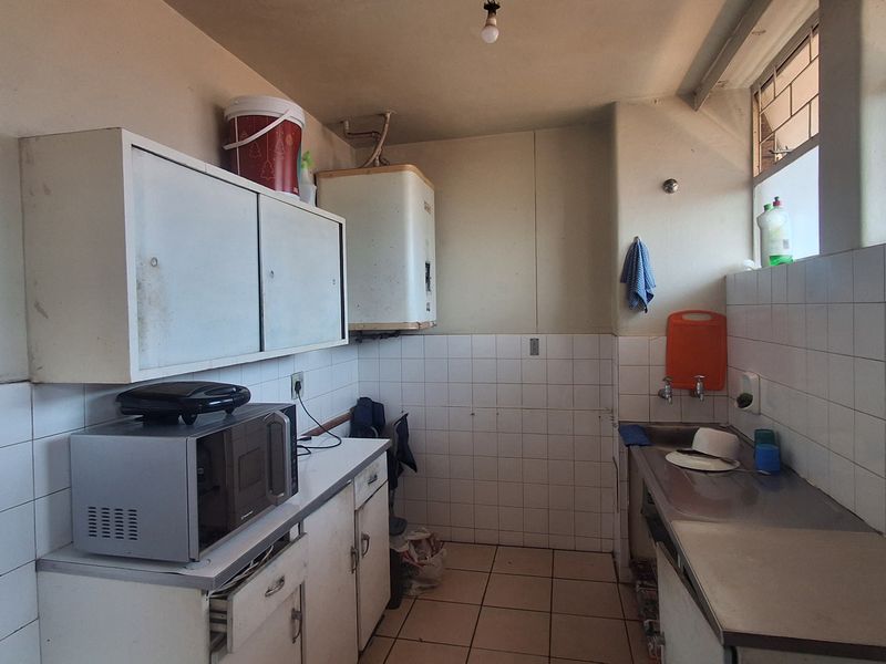 A functional kitchen area featuring tiled splashbacks, stainless steel sink, built-in cabinetry, and an electric geyser, requiring cosmetic updates to modernize the space.