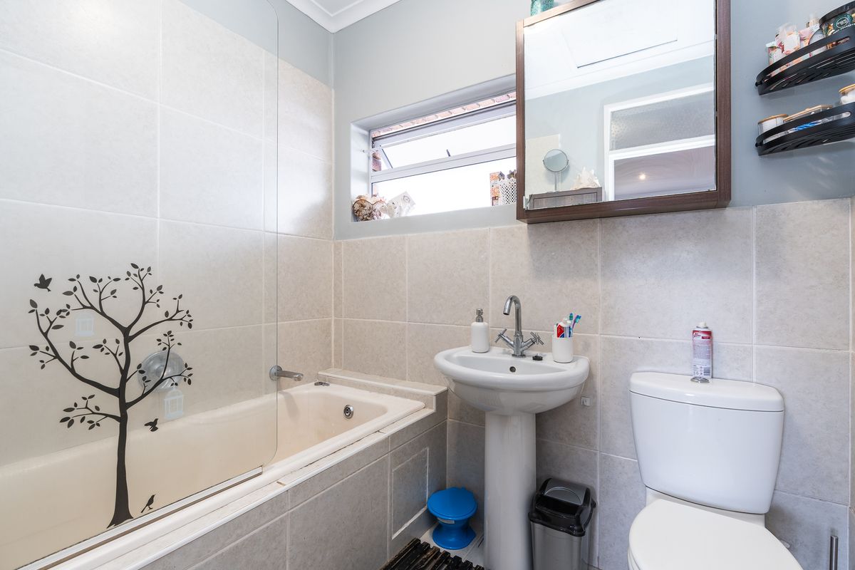 A functional bathroom featuring a pedestal basin, bathtub with a glass screen, toilet, and wall-mounted medicine cabinet with neutral tiled finishes.