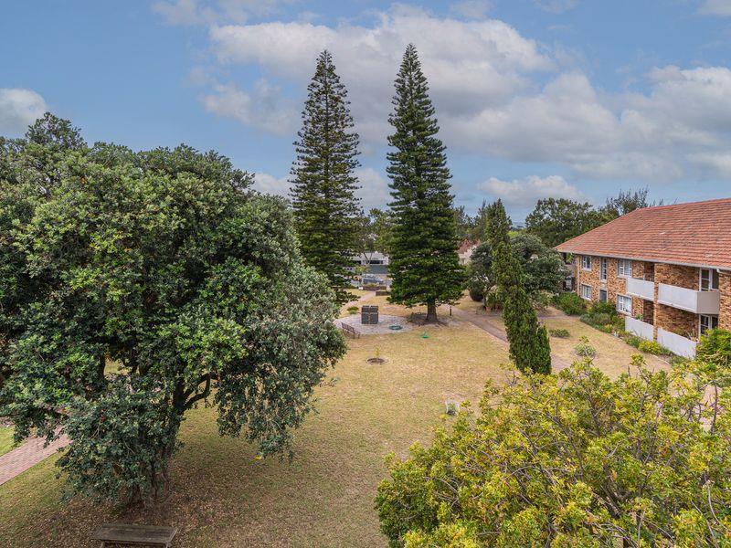 An elevated view of a communal garden area featuring mature trees, a paved walkway, and the exterior facade of a brick apartment building.