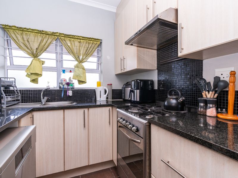 A functional kitchen featuring light wood-finish cabinetry, dark granite countertops, a gas hob with extractor fan, and a tiled backsplash.