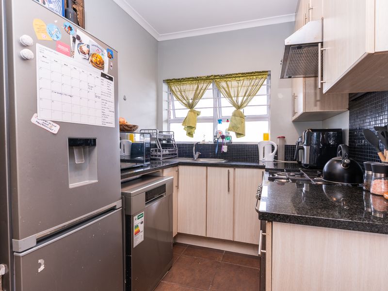 A functional kitchen featuring granite countertops, built-in cabinetry, a gas hob with extractor fan, and a tiled backsplash.