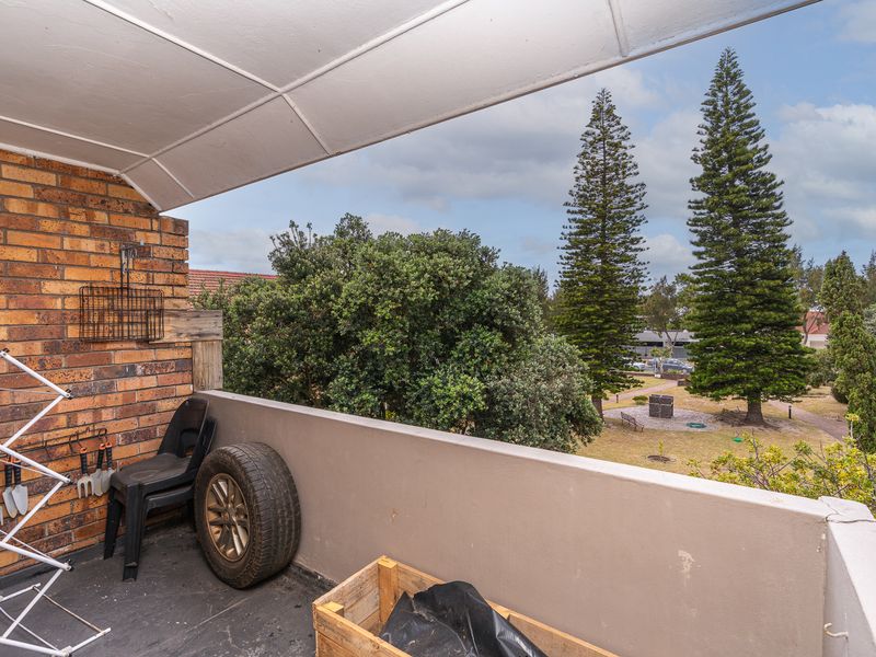 A covered balcony featuring a brick feature wall and concrete balustrade, offering an elevated view of the surrounding garden and trees.