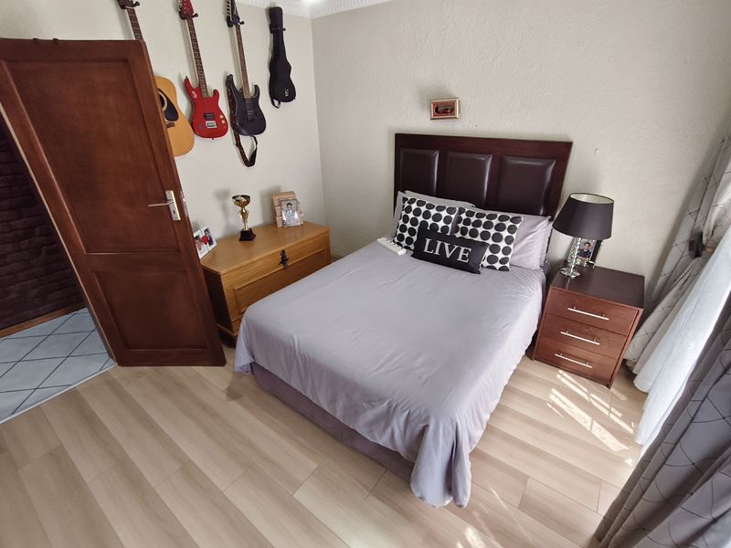 A well-maintained bedroom featuring light-toned laminate flooring, crown molding, and a solid wood door, providing a comfortable and functional living space.