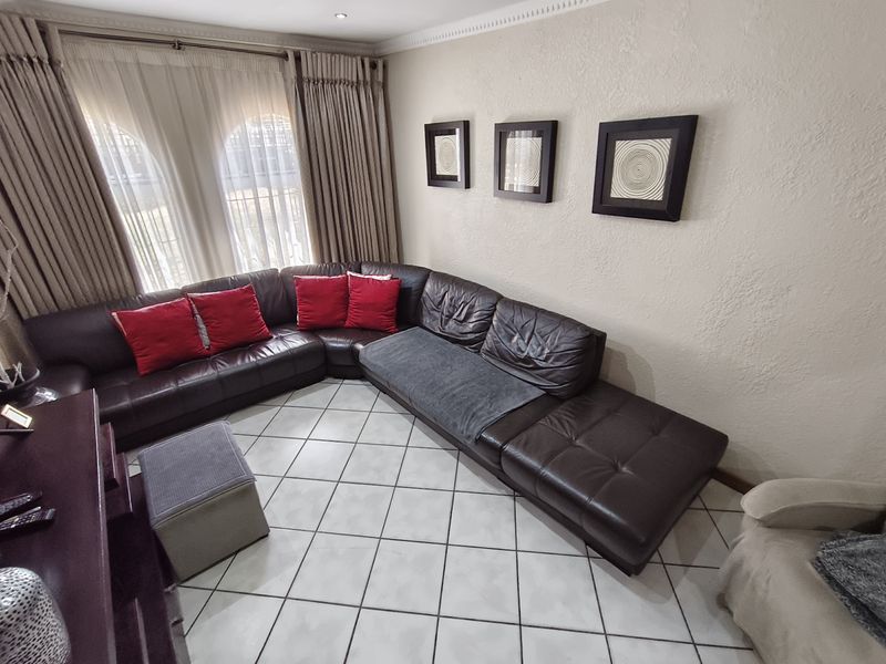 A comfortable living room featuring tiled flooring, recessed ceiling lighting, and arched windows with floor-to-ceiling curtains.