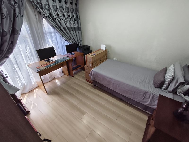 A functional bedroom featuring light-toned laminate flooring and a sliding glass door providing natural light.
