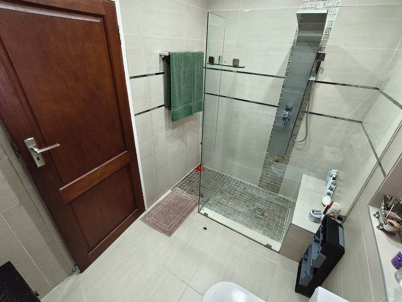 Modern bathroom featuring a walk-in shower with a glass screen, integrated shower panel, and built-in tiled bench.