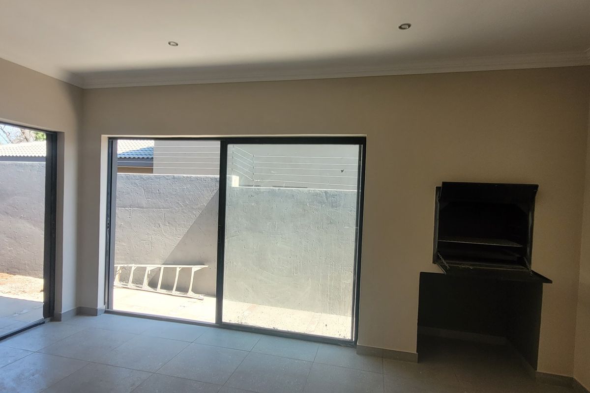 Spacious living area featuring tiled floors, recessed lighting, and a built-in braai, with large sliding doors providing direct access to the rear patio.