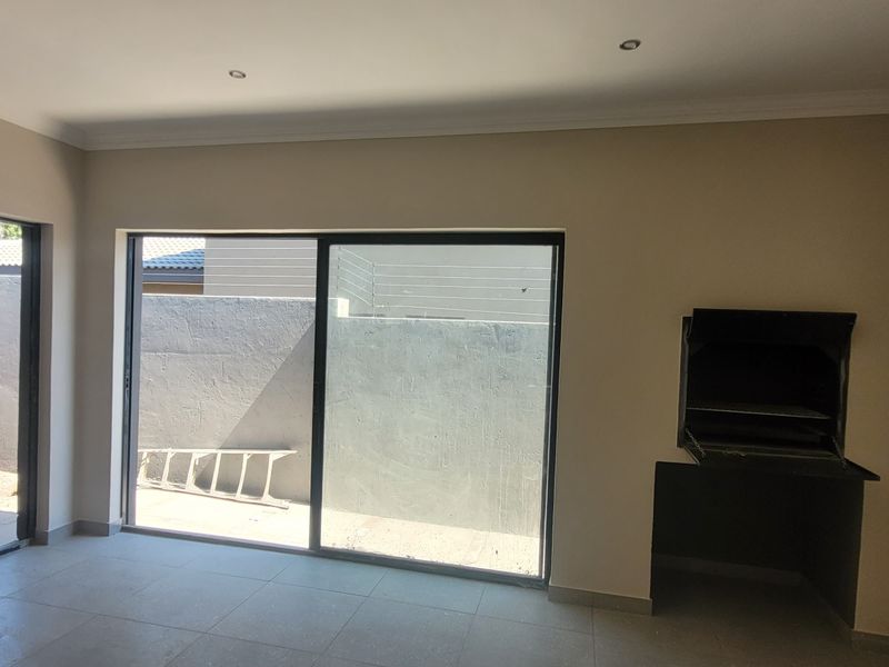 Spacious living area featuring tiled floors, recessed lighting, and a built-in braai, with large sliding doors providing direct access to the rear patio.