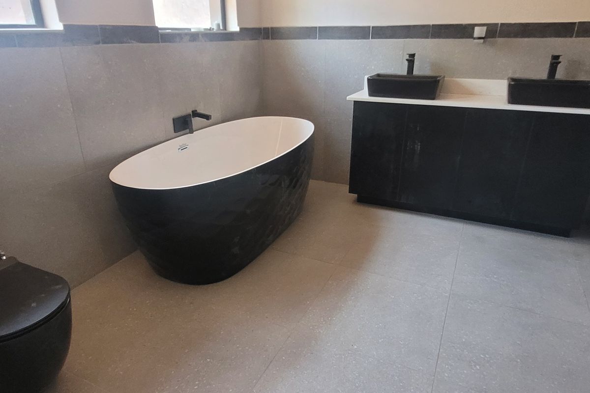 Modern bathroom featuring a sleek freestanding bathtub, a double vanity with dual vessel sinks, and contemporary grey tiling throughout.