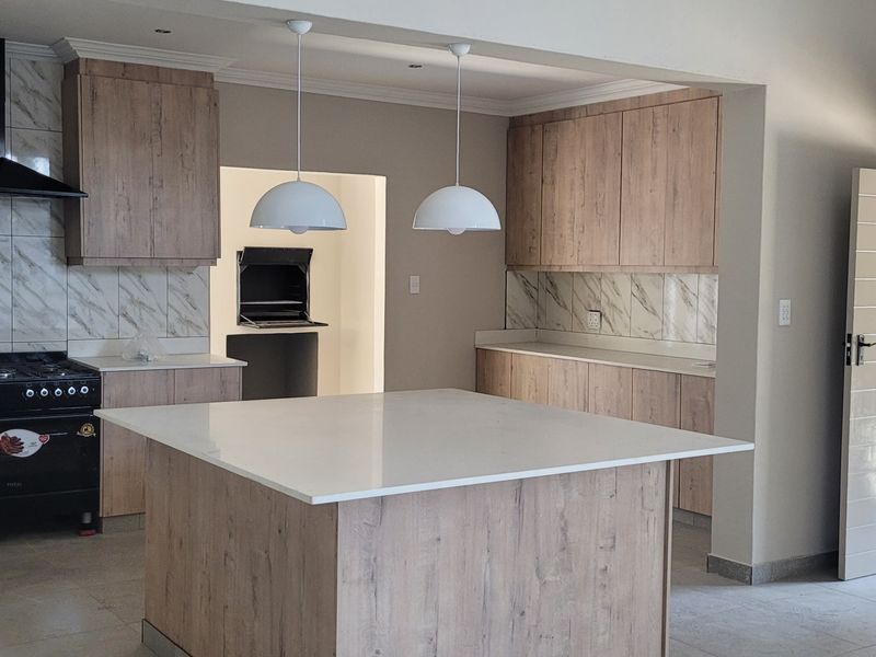 Modern kitchen featuring wood-finish cabinetry, stone countertops, a central island, gas stove, and a built-in braai area in the adjacent scullery space.