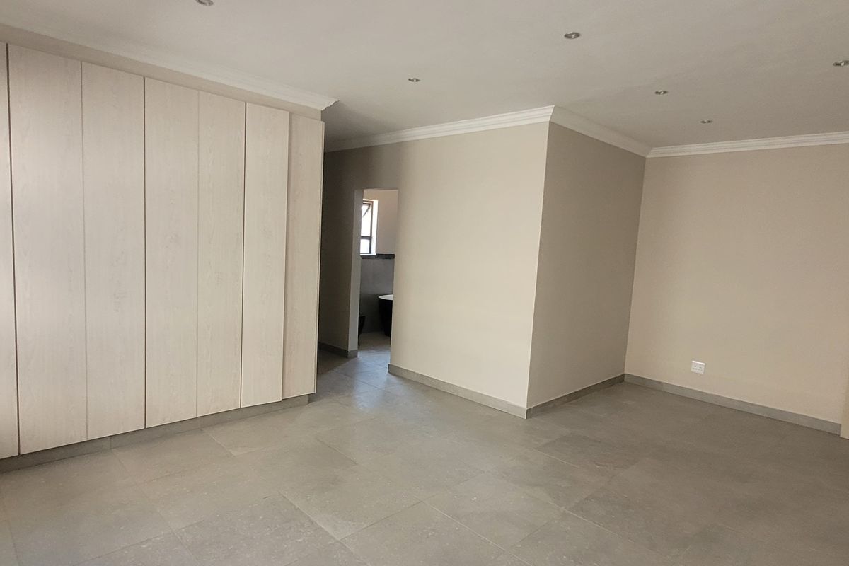 A spacious, empty bedroom featuring neutral tiled flooring, extensive built-in cupboards, recessed ceiling lighting, and a clean, modern finish.