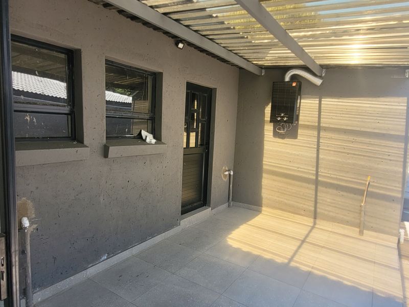 A covered outdoor patio area featuring tiled flooring, a gas geyser, and direct access to the home via a sliding door.