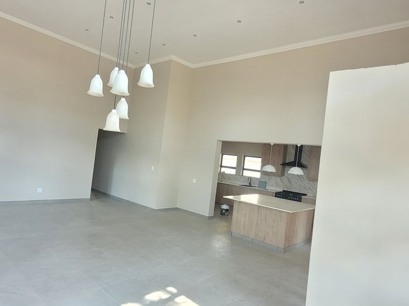 Spacious open-plan living area featuring high ceilings, tiled floors, and a modern kitchen with a central island and built-in appliances.