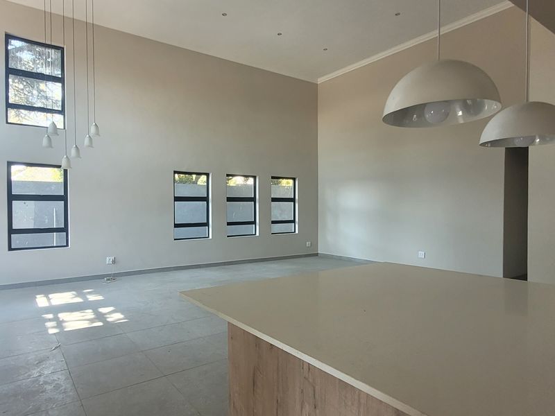 Spacious open-plan living area featuring double-volume ceilings, large windows, tiled flooring, and a central kitchen island with a stone countertop.