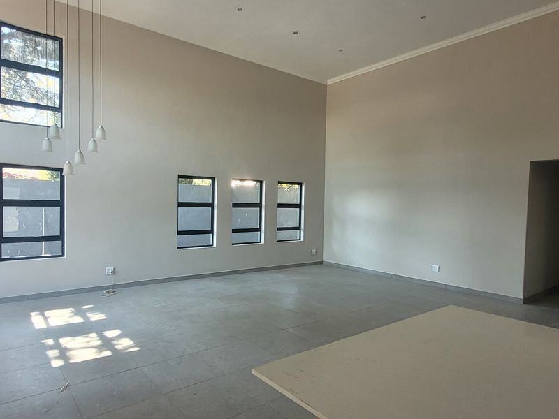 Spacious open-plan living area featuring double-volume ceilings, large aluminium-framed windows, tiled flooring, and a central kitchen island with pendant lighting.